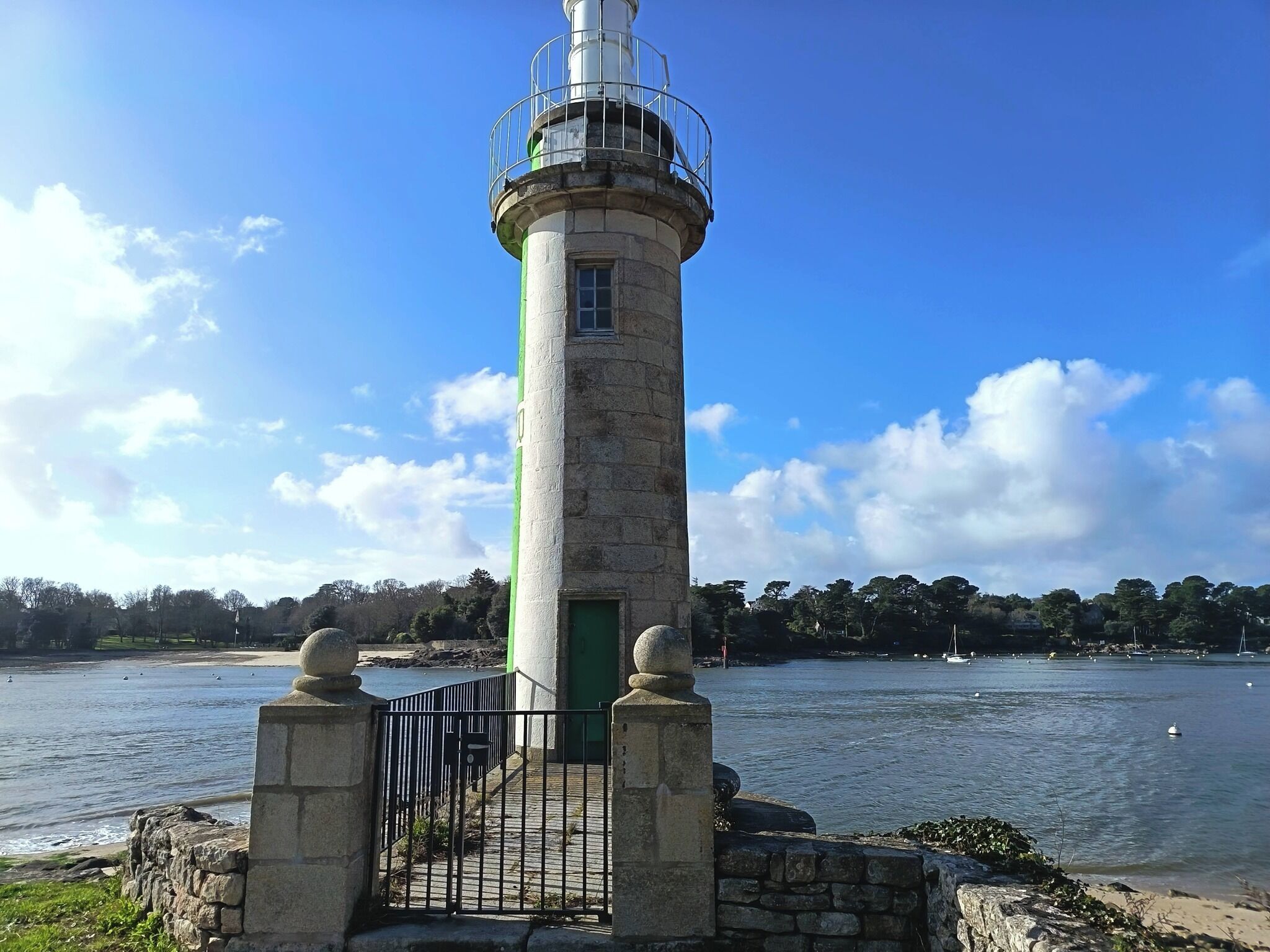 Un faro con base in pietra, ringhiera in metallo e una porta verde.