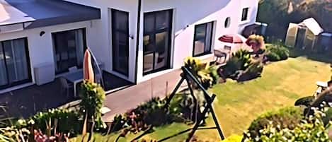 Una casa moderna de dos pisos con un patio, ventanas grandes y un jardín bien cuidado.