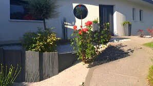 A modern building with a curved facade, a circular window, and a garden with red flowers.
