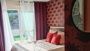 A bedroom with a bed, curtains, a view of the outdoors, and a patterned wall.