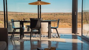 Un comedor moderno con una mesa y sillas, una lámpara colgante y vistas a un paisaje natural a través de grandes ventanales.