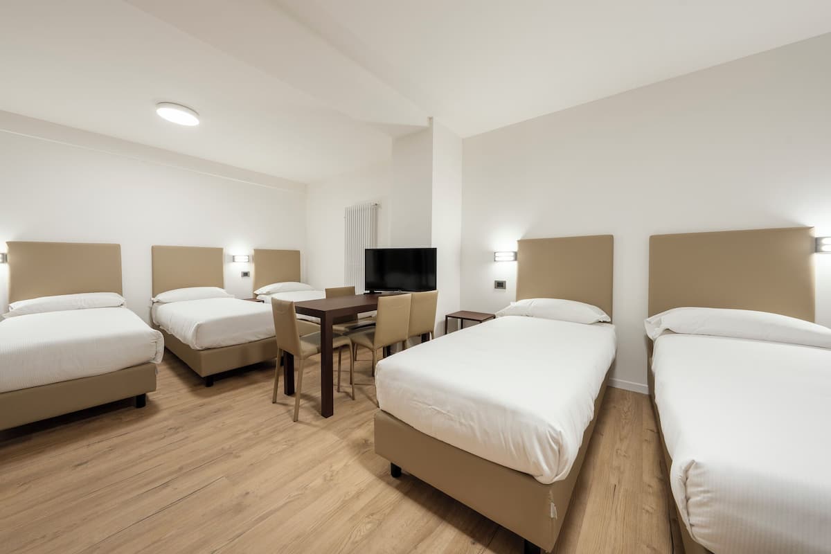 Ein Hotelzimmer mit vier Betten, einem Schreibtisch, einem Sessel, einem Fernseher und einer Heizung.