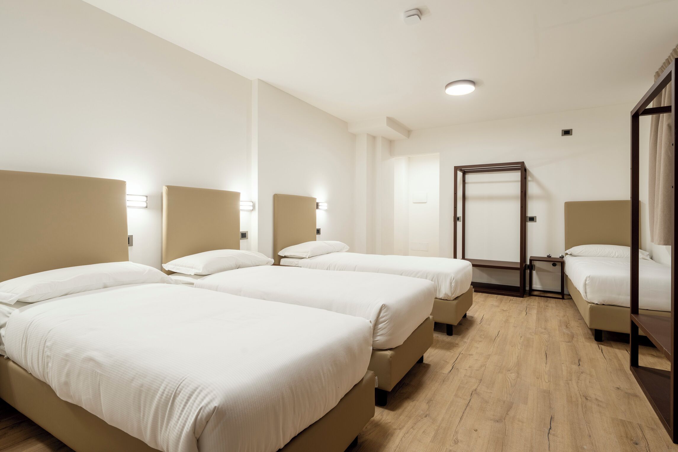 Une chambre d’hôtel avec trois lits, un plancher en bois et une porte dotée d’un miroir.