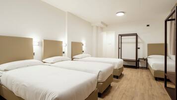 Ein Hotelzimmer mit drei Betten, Holzboden und einer Tür mit Spiegel.