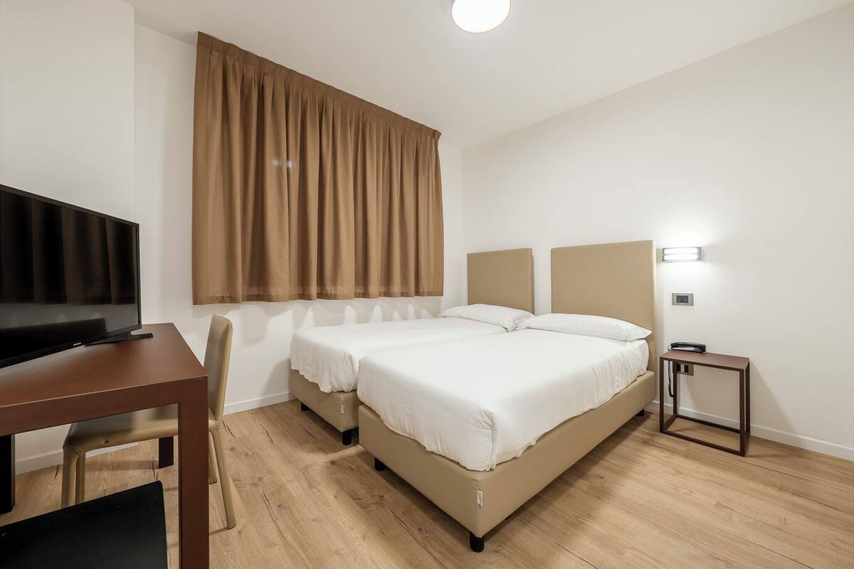 Ein Hotelzimmer mit Bett, Fernseher, Schreibtisch und Stuhl.