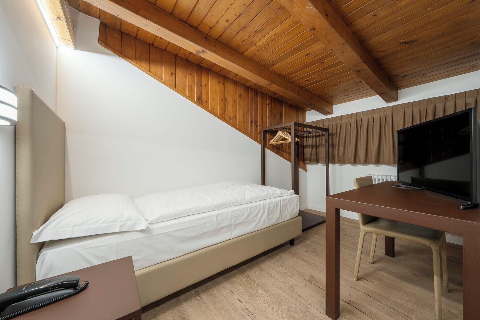 A bedroom with a bed, a desk, a television, and a hanging light fixture.
