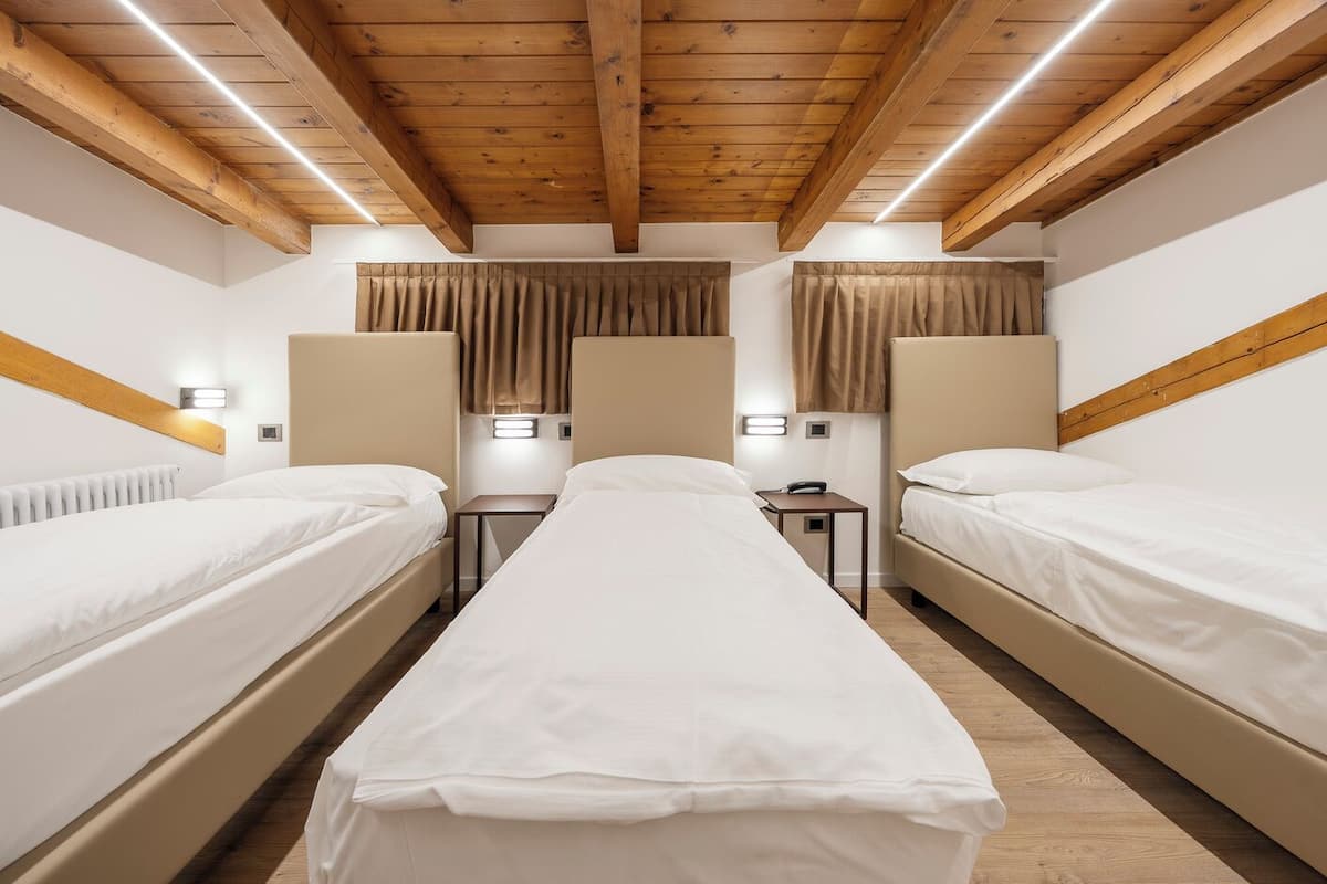 Ein Hotelzimmer mit zwei Einzelbetten, einem zentralen Bett, Holzbalkendecke und Nachttischlampen.