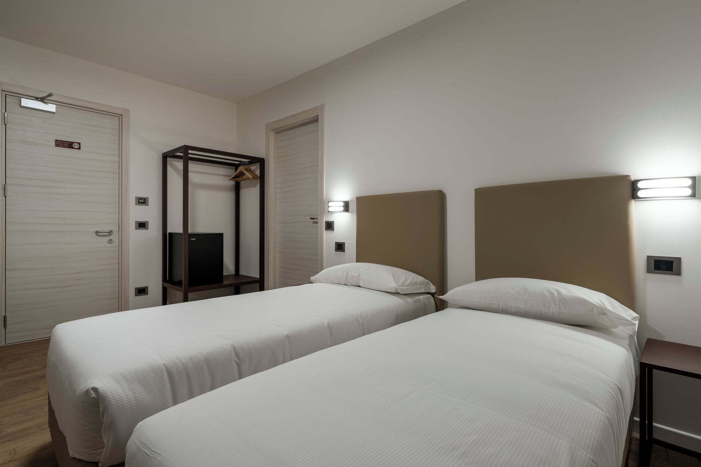 A hotel room with two single beds, a wardrobe, a mirror, and a small table.