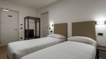 A hotel room with two single beds, a wardrobe, a mirror, and a small table.
