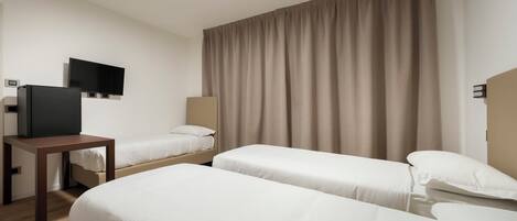 A hotel room with two single beds, a TV, a desk, and a large window with curtains.