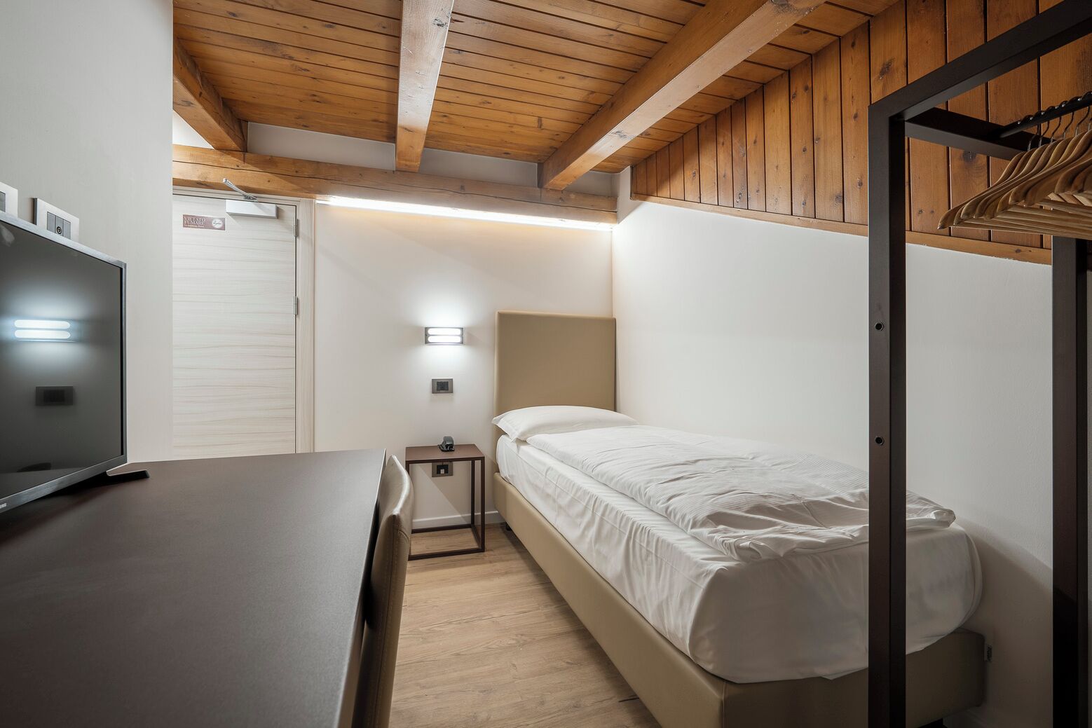 Una habitación de hotel pequeña con cama, mesita de noche y televisión.