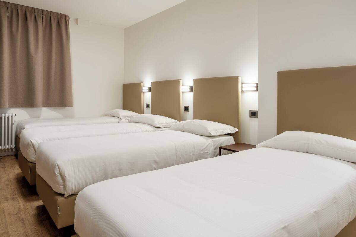 Ein Hotelzimmer mit drei Betten, einem Heizkörper und Wandleuchten.