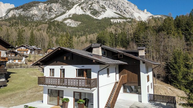 Una casa moderna de dos pisos con balcón, ventanas amplias y una escalera que conduce al nivel superior.