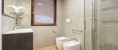 A modern bathroom with a shower, toilet, bidet, and a sink with a mirror above.