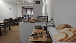 Un área de desayuno con mesas, sillas, una barra de buffet y una cocina con utensilios.