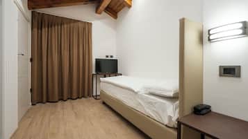 Een kleine eenpersoonskamer met een houten plafond, een televisie op een standaard, een nachtkastje en een wandlamp.