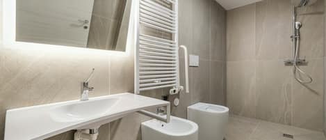 A modern bathroom with a white sink, a towel rack, a bidet, and a shower.