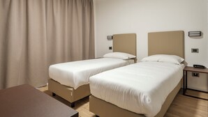 Habitación de hotel con dos camas, un escritorio, una mesita de noche y un ventanal grande con cortinas.