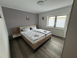 Ein Schlafzimmer mit Bett, Fenster, Heizkörper und einer kleinen Pflanze.