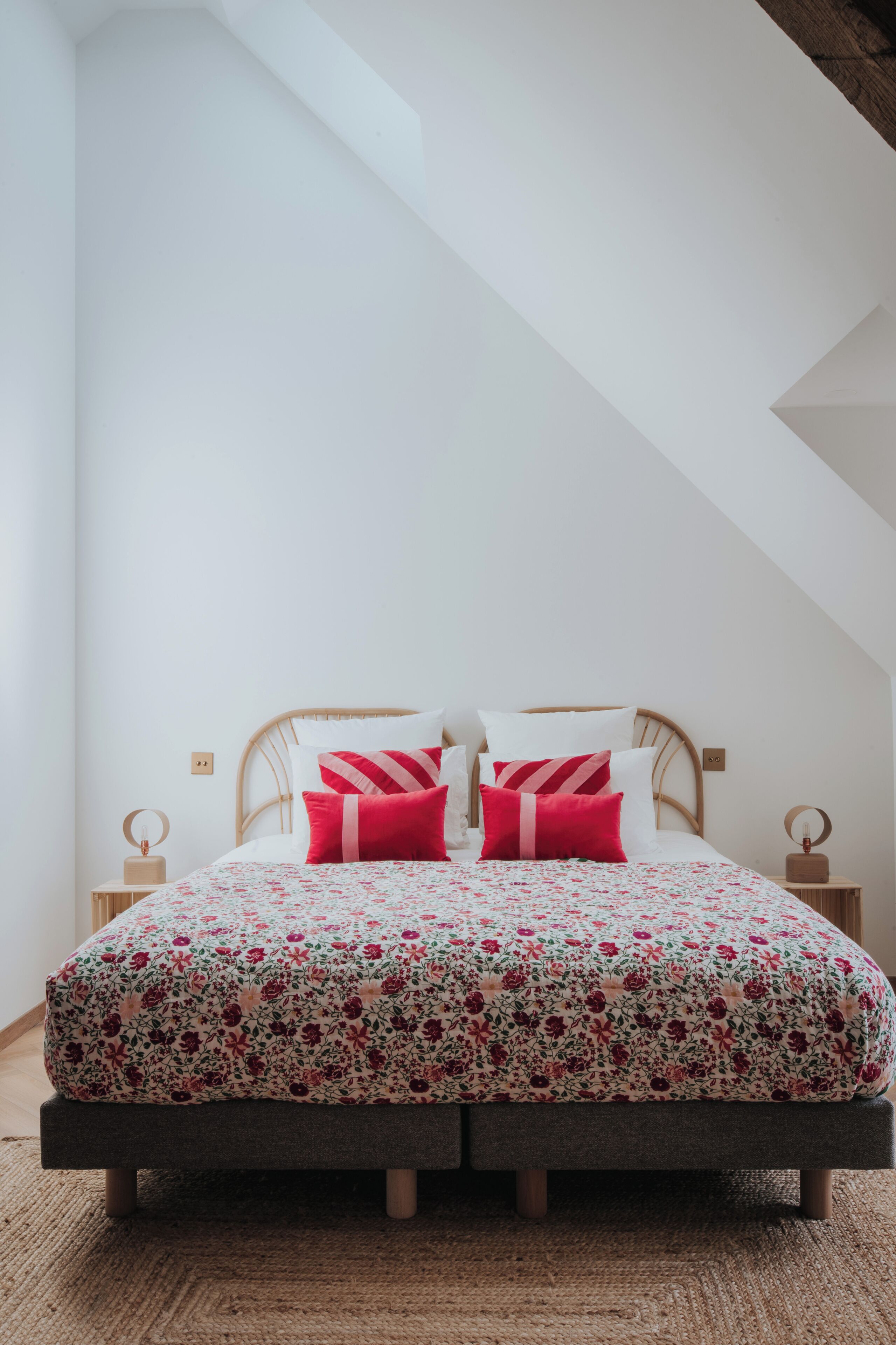 A bed with a floral bedspread and two red pillows in a room with white walls and a sloped ceiling.