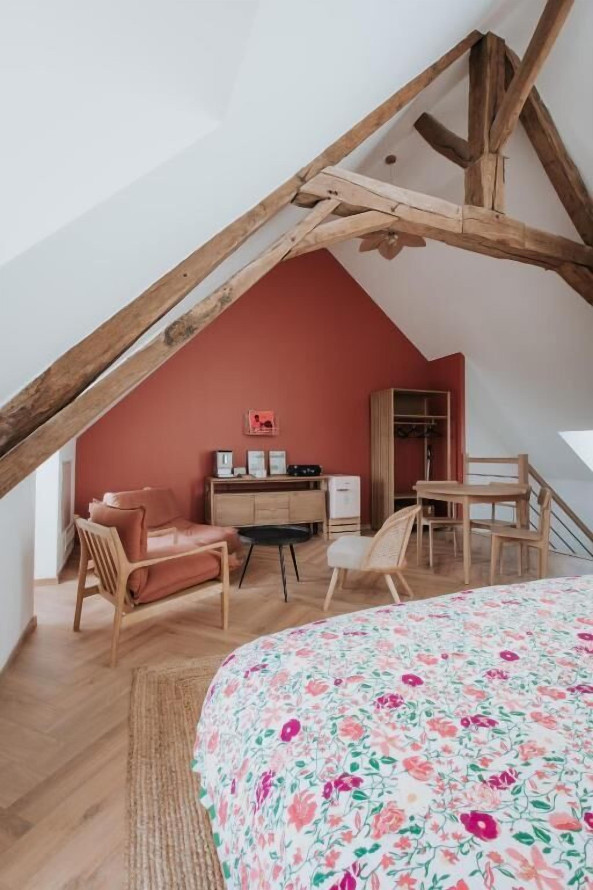 Un dormitorio con techo inclinado, una cama con colcha estampada, un escritorio con silla, un armario y una pared roja decorativa.