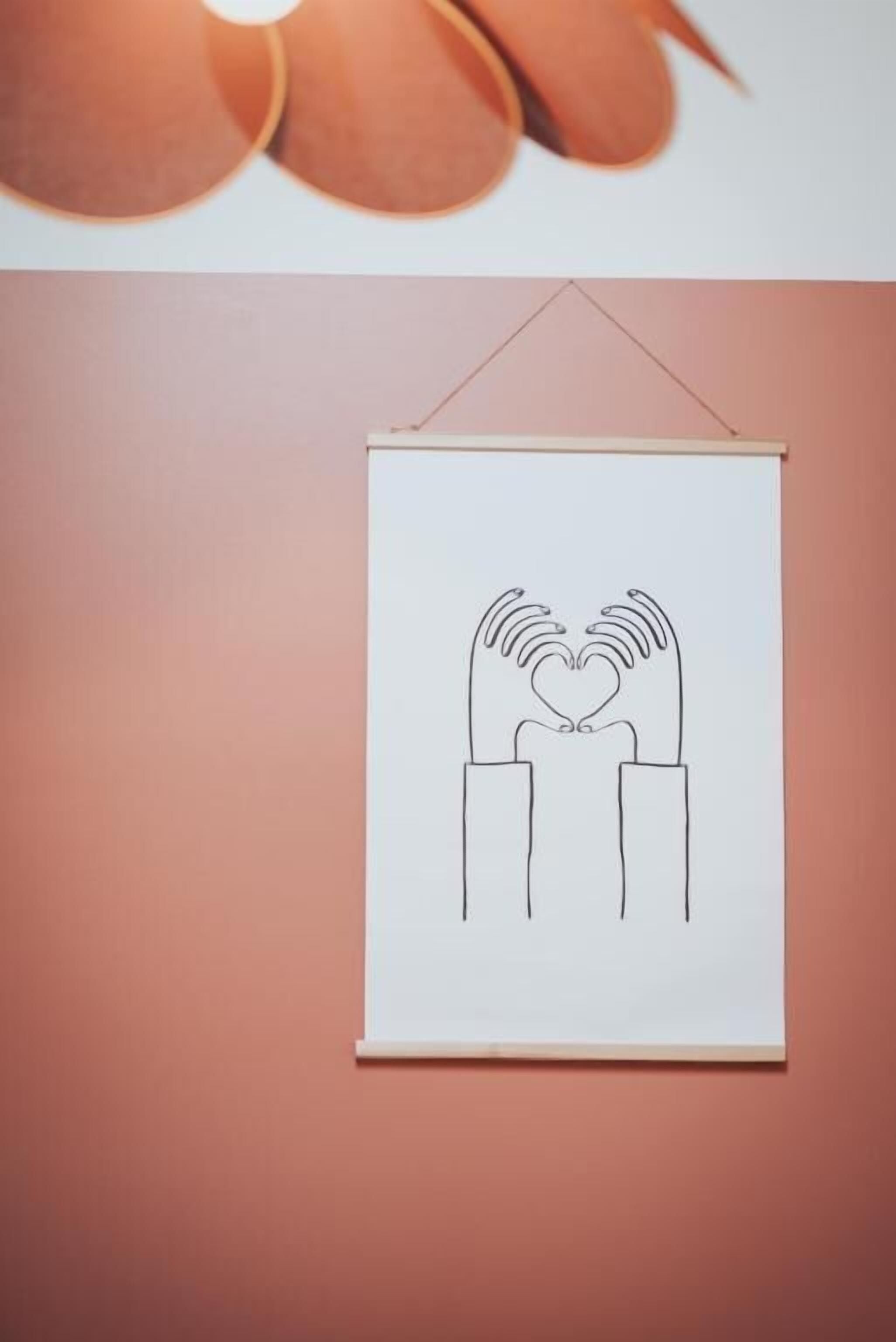 Un disegno incorniciato raffigura mani che formano un cuore su un muro.
