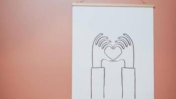 Un disegno incorniciato raffigura mani che formano un cuore su un muro.