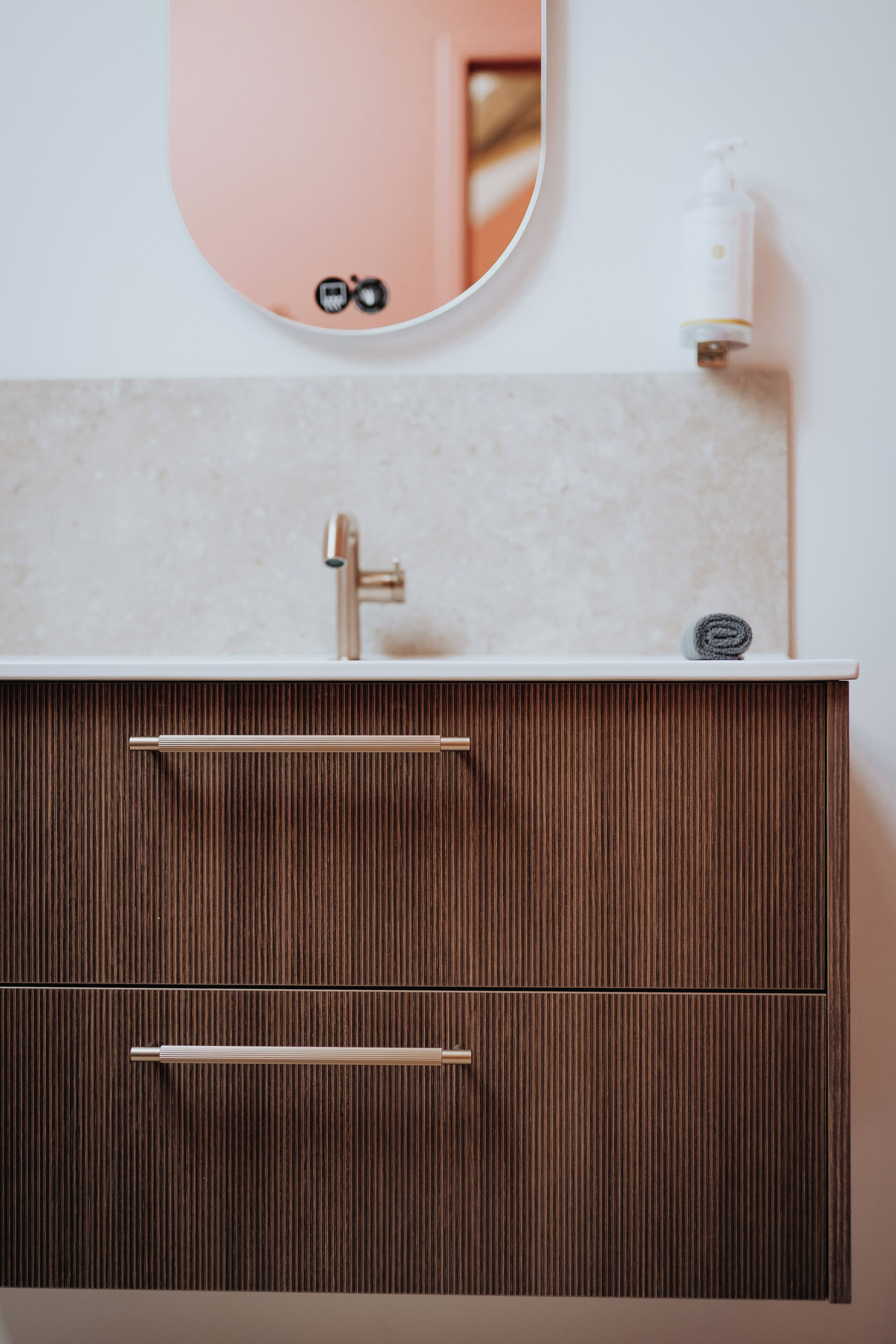 Un baño con lavamanos blanco, un espejo, una toalla y un dispensador de jabón.