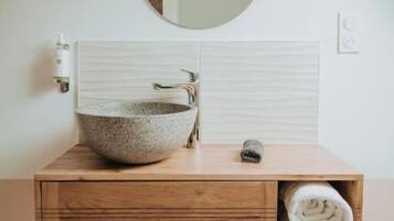 Un baño con un espejo redondo, un lavabo de piedra, tocador de madera y toallas.
