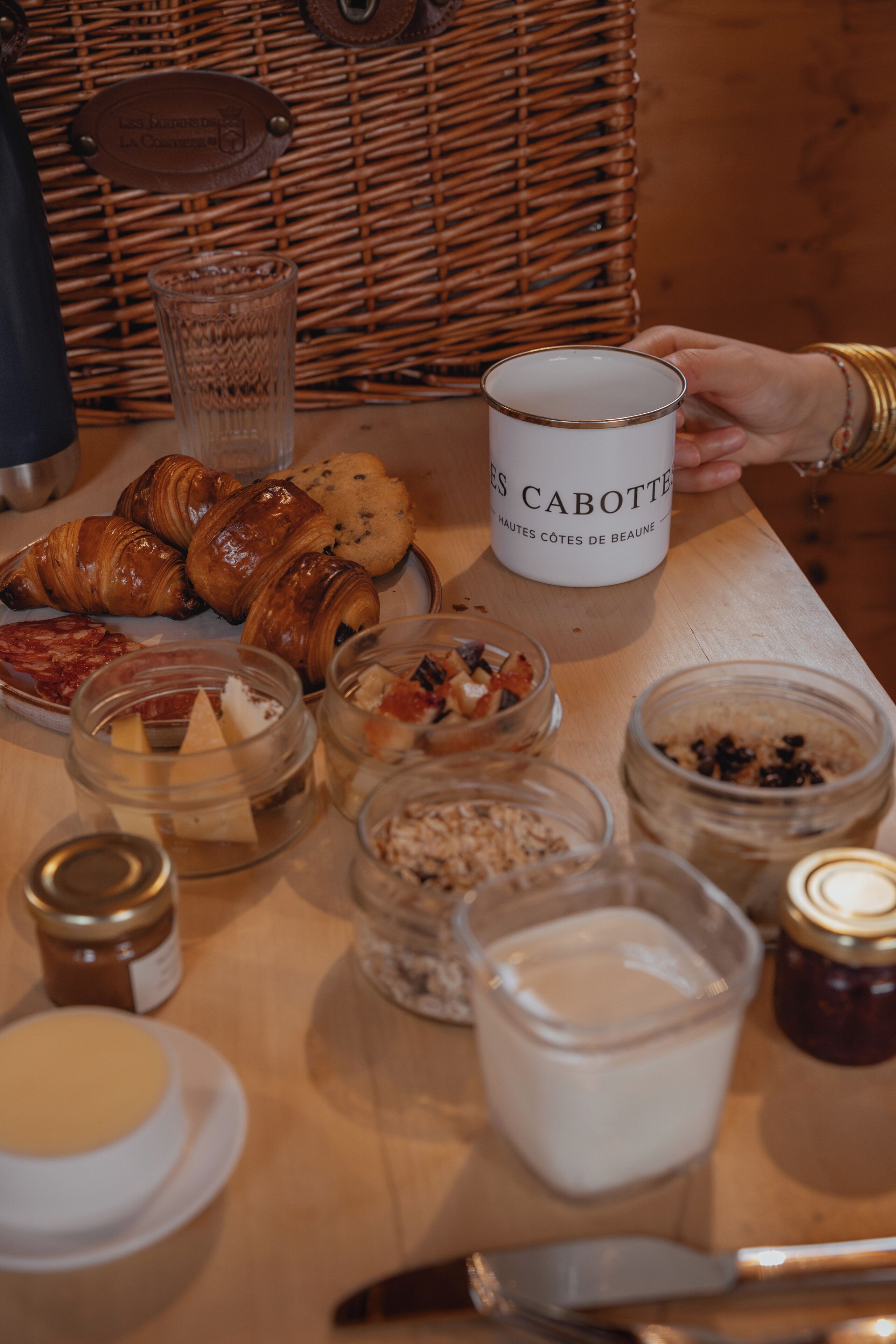 Una mesa de desayuno con pasteles, una vela con la etiqueta 'LES CABOTTE' y varios frascos de mermeladas y salsas.