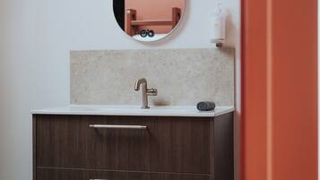 Un baño moderno con encimera de mármol, lavamanos empotrado en la pared, un espejo grande y un mueble de tocador de madera oscura con cajones.