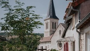 Ein Innenhof mit rundem Tisch und Stühlen, Topfpflanzen, einer Kirche mit hohem Turm und einem Gebäude mit Ziegeldach.