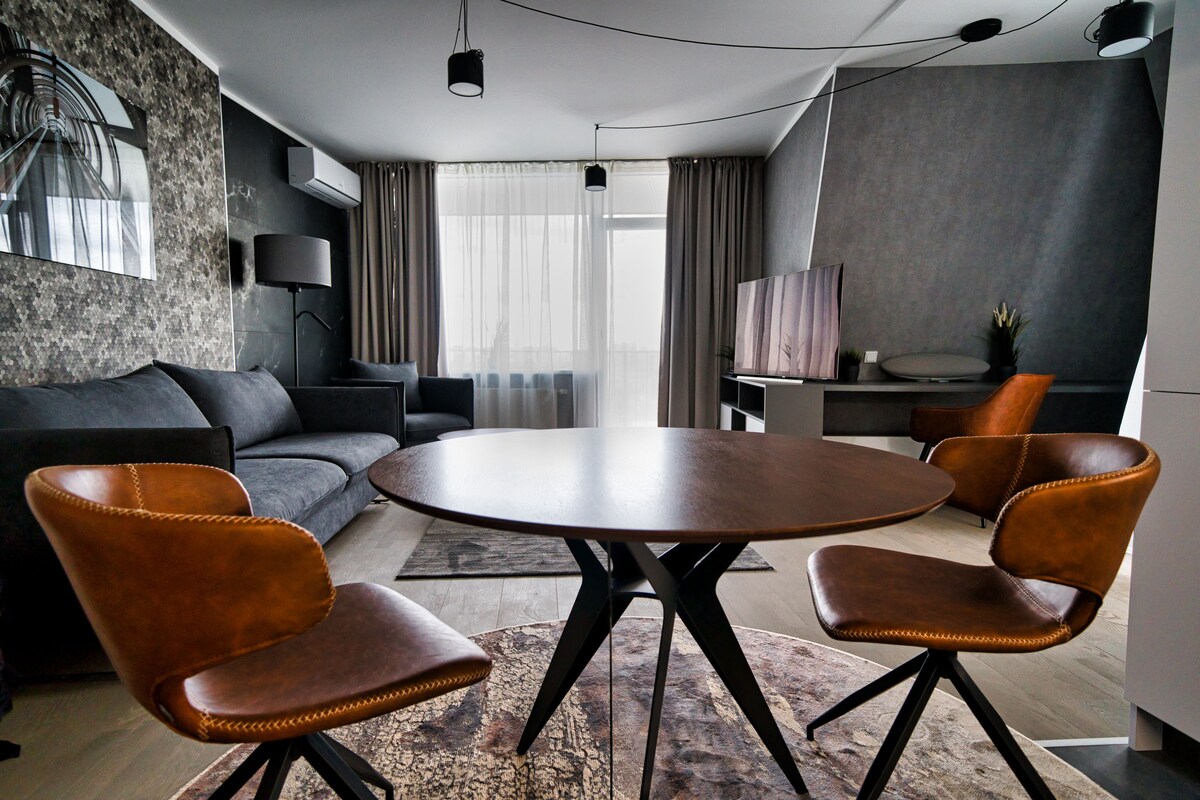 A modern living room with a round table, two leather chairs, a sofa, and a television.