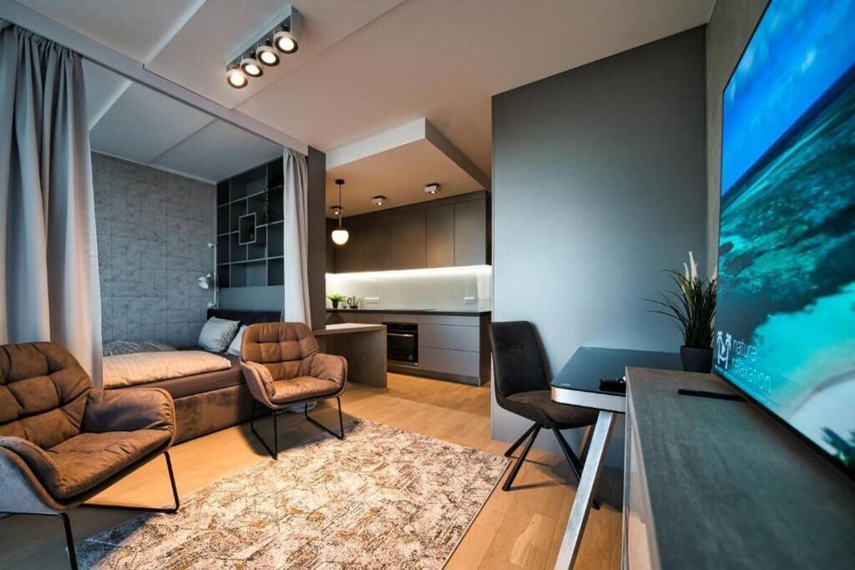 Un salon moderne comprenant un canapé, des fauteuils, un téléviseur et un coin cuisine.