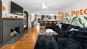 Uma sala de estar moderna com lareira, cozinha ao fundo e um mural na parede.