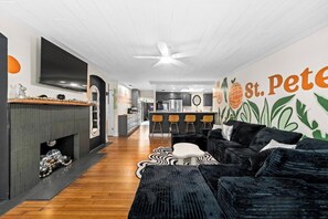 A modern living room with a fireplace, a kitchen in the background, and a wall mural.