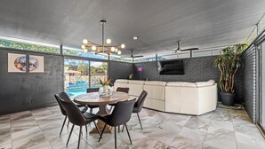Uma sala de estar moderna com piscina, área de jantar e televisão presa a uma parede de tijolos.