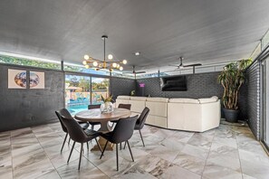 A modern living room with a pool, a dining area, and a TV mounted on a brick wall.