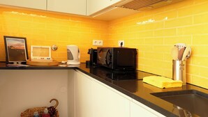 Cozinha com bancada preta, cafeteira, micro-ondas e cesta com garrafas.