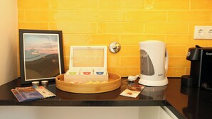 Uma bancada de cozinha com uma cafeteira, um quadro emoldurado, uma bandeja com xícaras e uma pequena mesa com revistas.