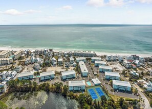 Luftaufnahme eines Küstenresorts mit mehreren Gebäuden, einem Strand und einem Tennisplatz.