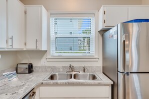 Eine Küche mit weißen Schränken, einem Edelstahlkühlschrank, einer Spüle mit zwei Becken und einem Fenster mit Jalousien.