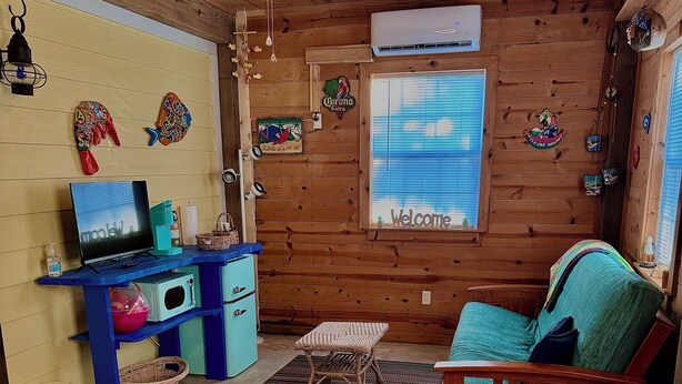 Ein Zimmer mit einem Bett, einem Schreibtisch, einem Stuhl, einem Deckenventilator und einem Fenster mit einem 'Welcome'-Schild.