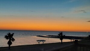 Ein Sonnenuntergang über einem ruhigen Meer mit Strand und Palmen.