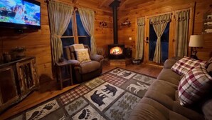 Interior acogedor de una cabaña con chimenea, paredes de madera, un televisor y una alfombra estampada de cuadros.