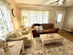 A living room with a brown sofa, a beige armchair, a white coffee table, a patterned rug, a potted plant, and a wall clock. - Blue Bungalow (Cedar Rapids)