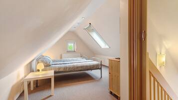 Une chambre avec un plafond en pente, un lit, une table de chevet avec une lampe, une fenêtre et une armoire en bois.