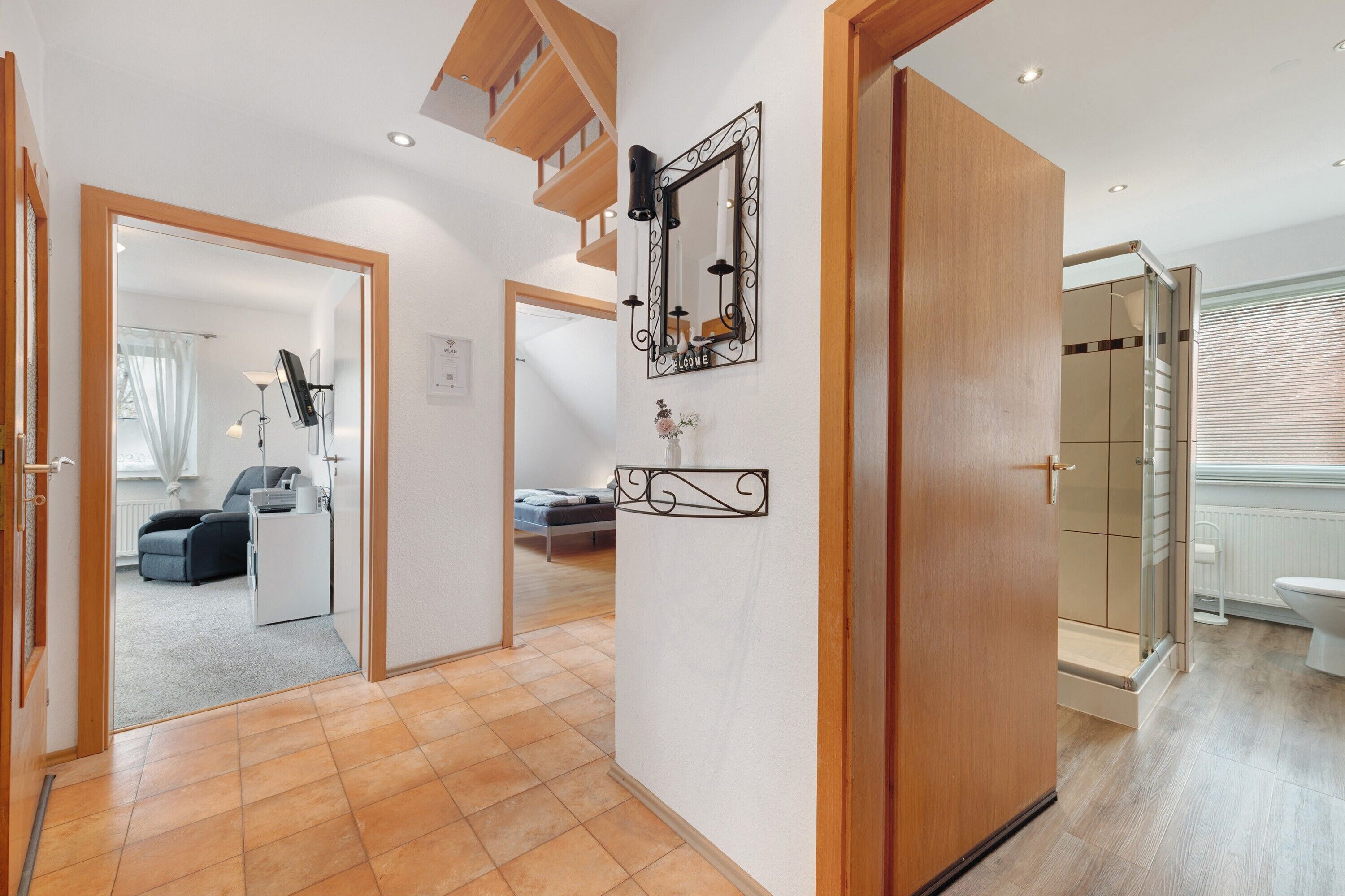 A hallway leading to a bedroom with a bed, a bathroom with a toilet, and a shower area.