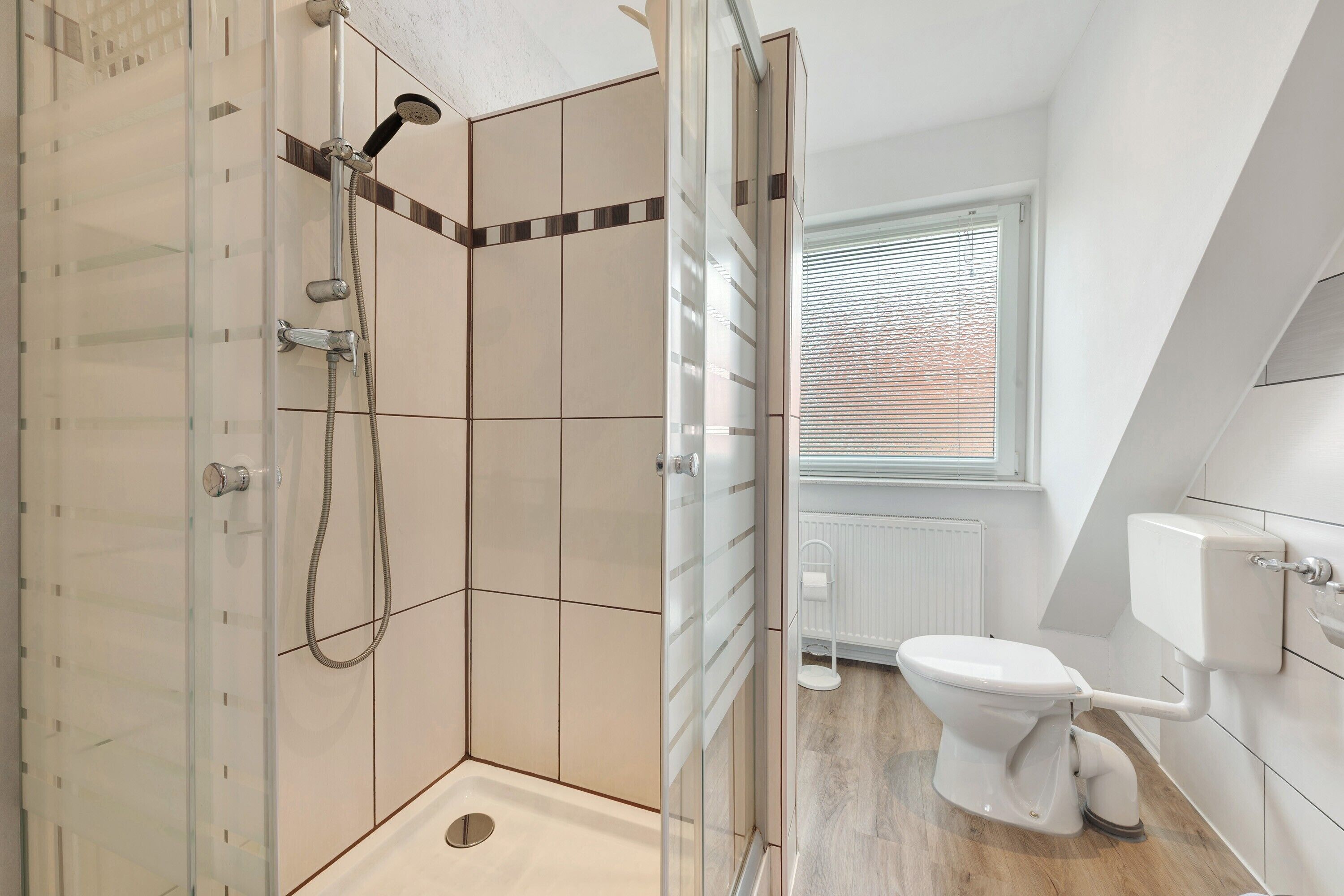 Une salle de bain moderne avec une douche à parois de verre, des toilettes et une fenêtre équipée de stores.