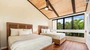 Une chambre avec deux lits, des têtes de lit en bois, un plafond en pente et une grande fenêtre donnant sur un paysage verdoyant.